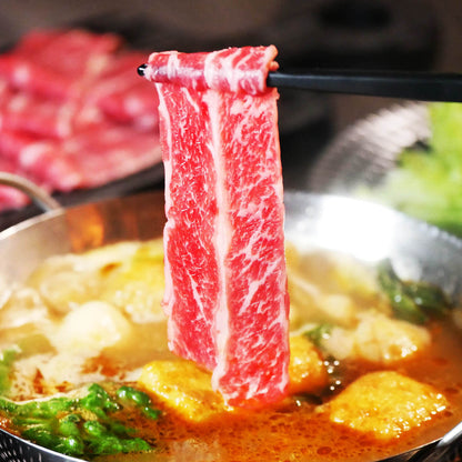Raw marbled beef strip on chopsticks over a hot pot with vegetables and broth.