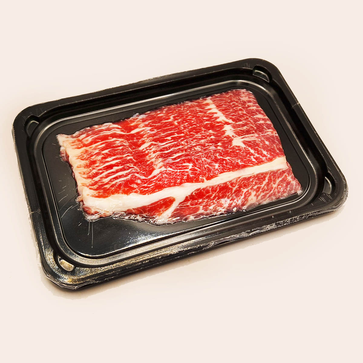 Raw beef with white marbling on a black plastic tray against a beige background