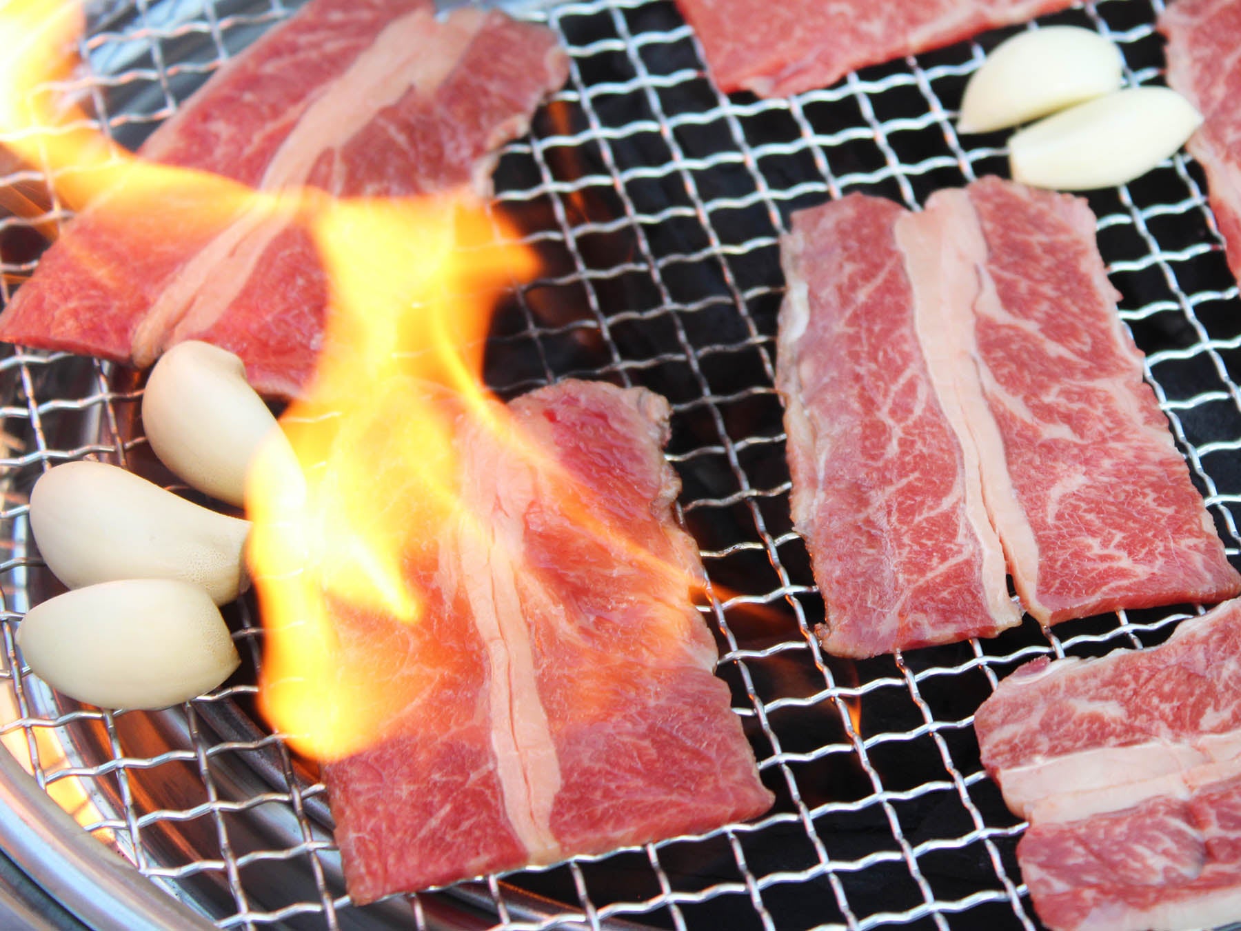 Raw beef slices and garlic on a grill with flames