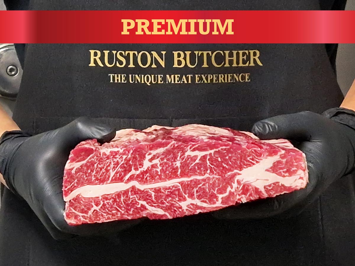 Person holding a piece of short rib with 'Ruston Butcher' branding in the background.